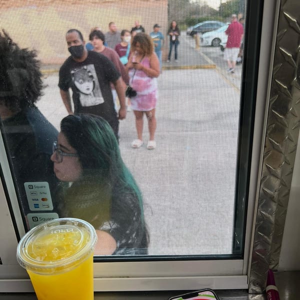 A refreshing yellow drink on a counter, with people waiting outside a food truck window.