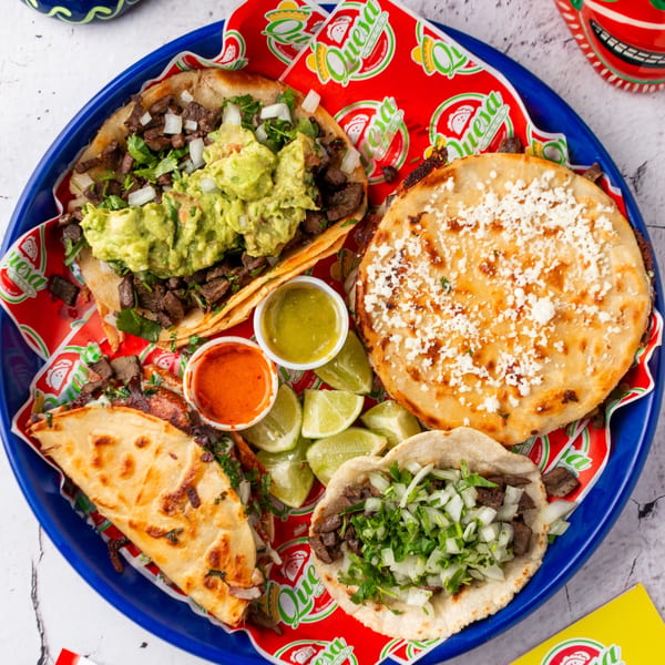 A blue platter of Quesa Loco tacos, a gordita, lime wedges, and two sauces.