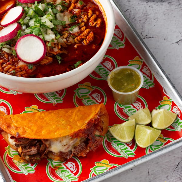 Quesa Loco birria ramen with radishes and onions, a cheesy birria taco, salsa, and lime wedges.
