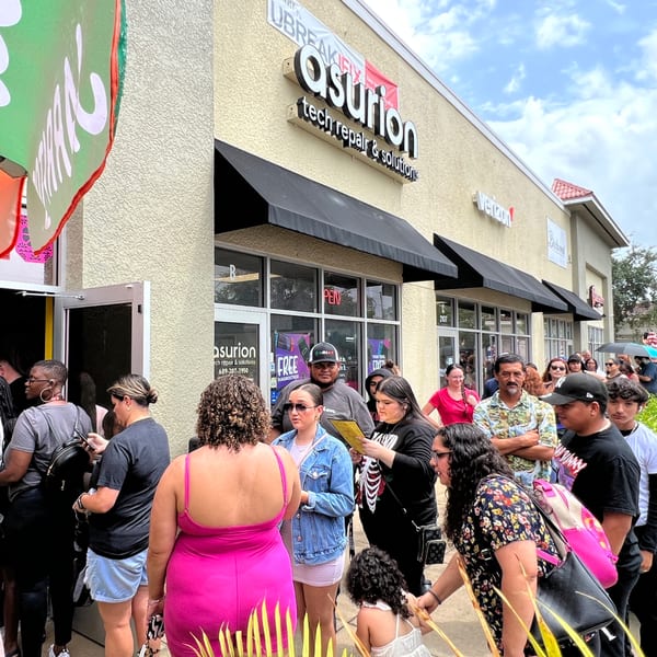 A large crowd of people gathered outside a building with an "Asurion" sign, likely waiting for Quesa Loco.