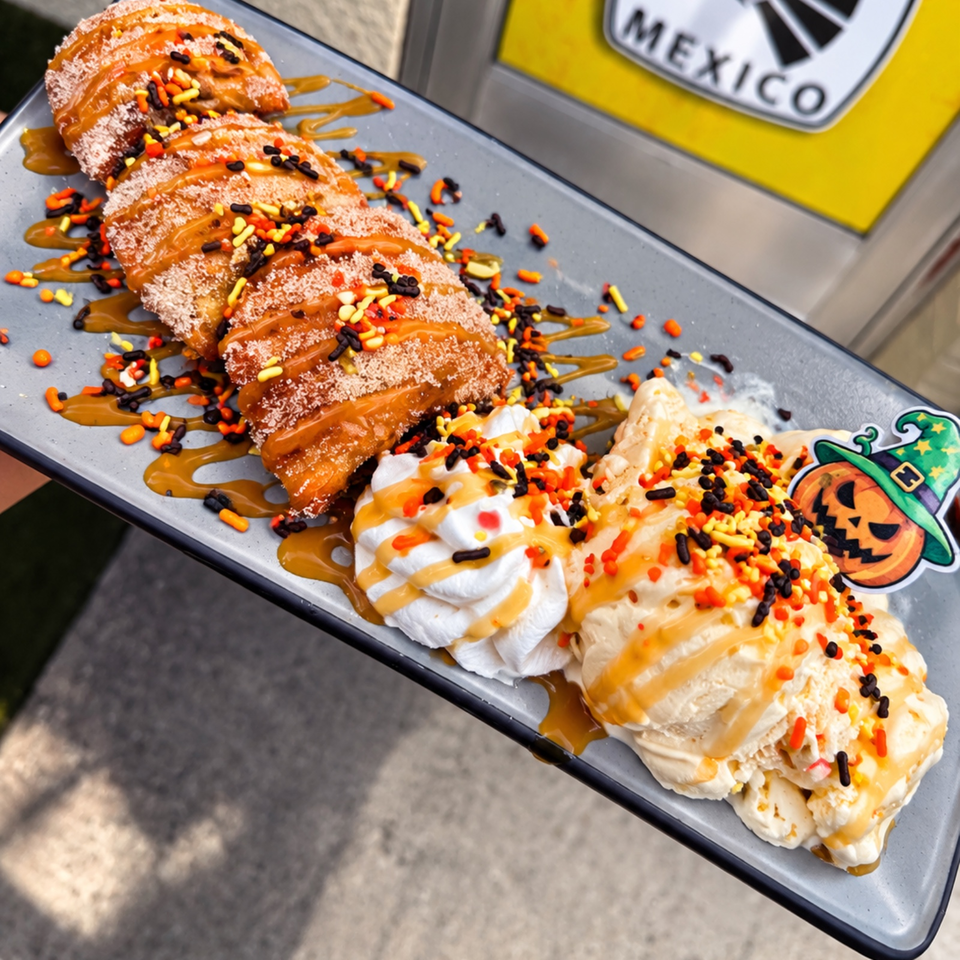 Plate of caramel-drizzled pastries topped with whipped cream and colorful sprinkles beside a Halloween-themed decoration.