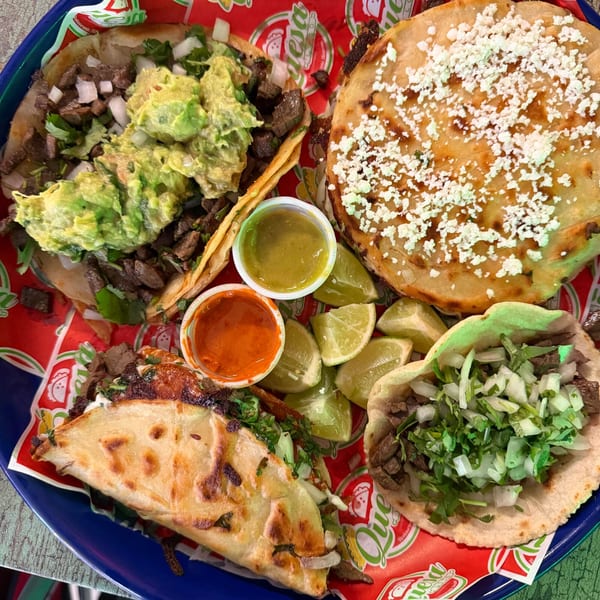 A vibrant platter of Quesa Loco tacos, including carne asada, guacamole, and a quesadilla, with lime and sauces.