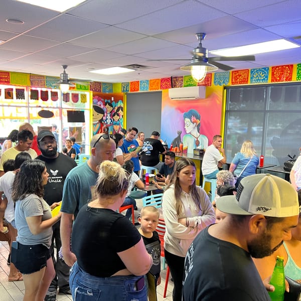 A crowded Quesa Loco restaurant with patrons waiting in line and seated at tables amidst colorful decor.