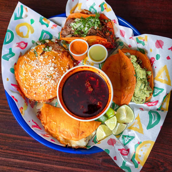 A blue plate filled with various Quesa Loco Mexican dishes, including tacos, quesadillas, and dipping sauces.
