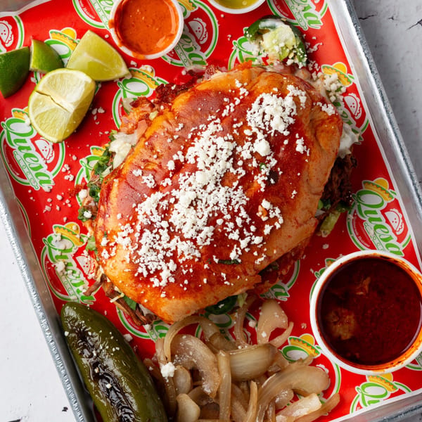 A Quesa Loco torta with red sauce and cheese, served with limes, grilled pepper, and onions.