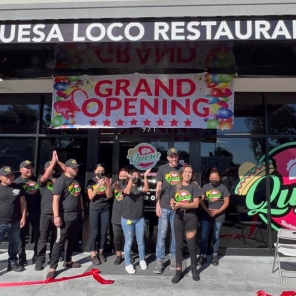 Quesa Loco staff celebrating grand opening with a red ribbon and banner outside the restaurant.