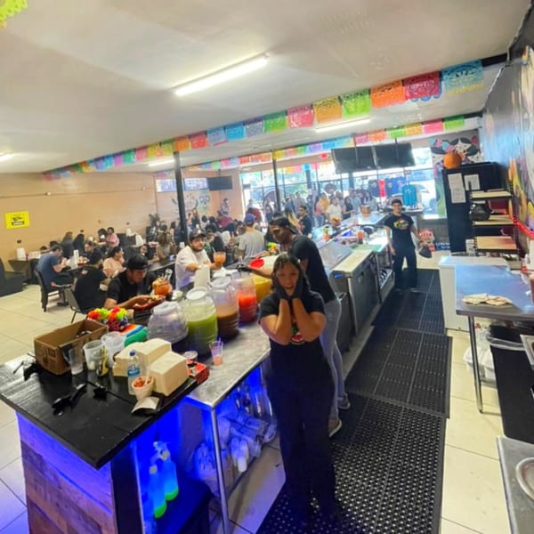 A bustling Quesa Loco restaurant interior with customers dining and staff behind a counter with colorful drinks.