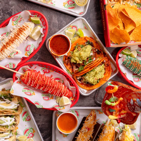 A vibrant spread of Quesa Loco's Mexican dishes, including tacos, elotes, nachos, and a michelada.