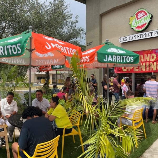 Patrons gather under Jarritos umbrellas at Quesa Loco's outdoor seating area, with a "Grand Opening" banner visible.