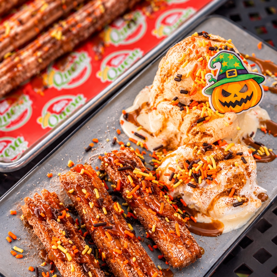 Halloween-themed churros with chocolate sauce, whipped cream, colorful sprinkles, and a pumpkin witch decoration on a serving tray.