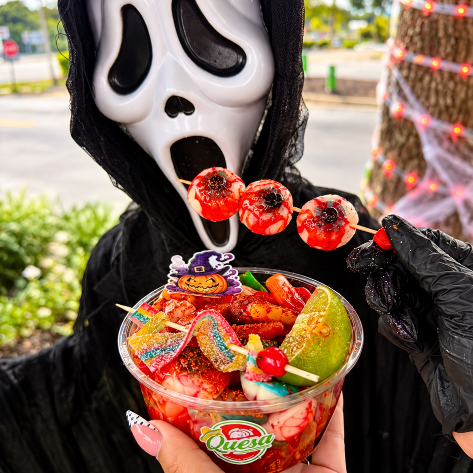 Person in a Ghostface costume holds a colorful cup of Mexican-style candy and fruit topped with red candy apples.