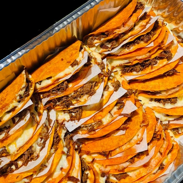 A catering tray filled with many Quesa Loco birria tacos, featuring orange tortillas, melted cheese, and shredded beef.