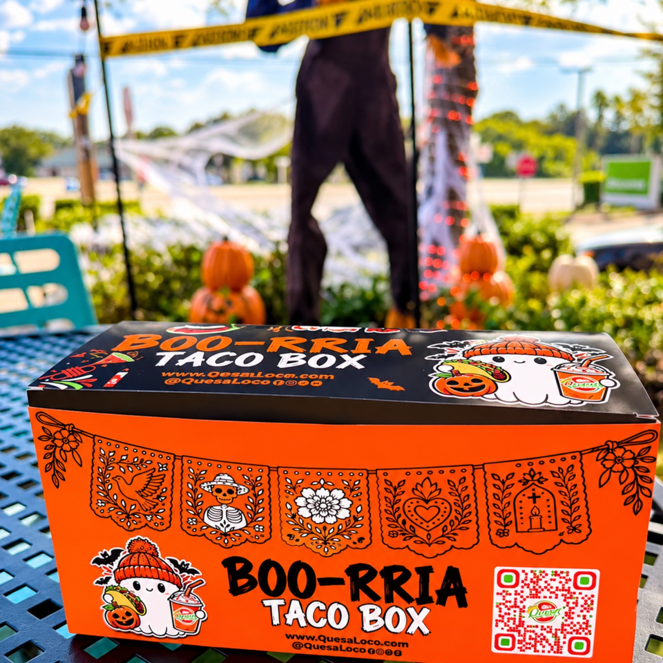 Orange Boo-Rria Taco Box with Halloween-themed illustrations on an outdoor table, pumpkins and caution tape in the background.