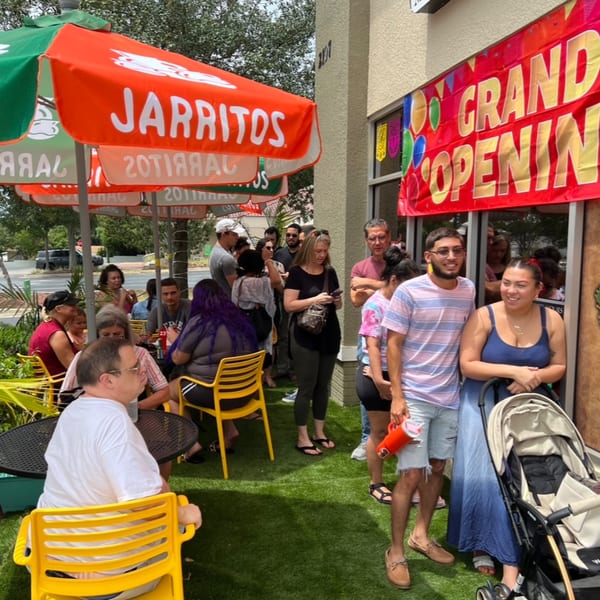 Customers gather outside Quesa Loco under Jarritos umbrellas and a "Grand Opening" banner.