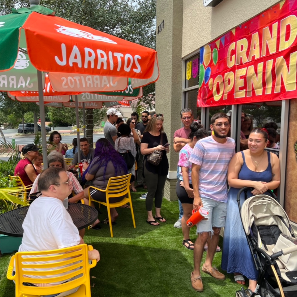 Customers gather outside Quesa Loco under Jarritos umbrellas and a "Grand Opening" banner.