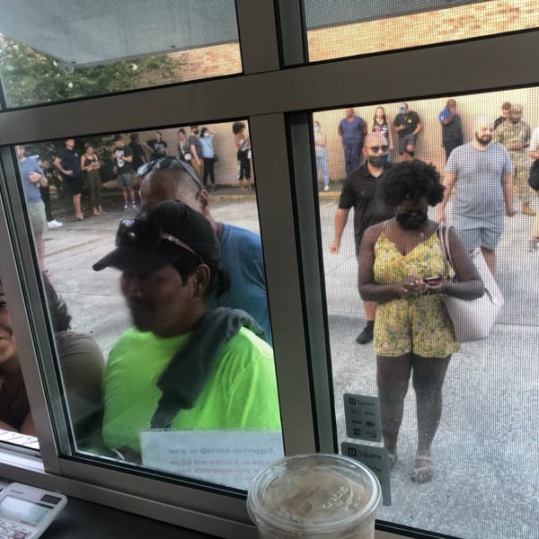 Customers wait in line outside Quesa Loco, viewed through a screened window with a drink and calculator.