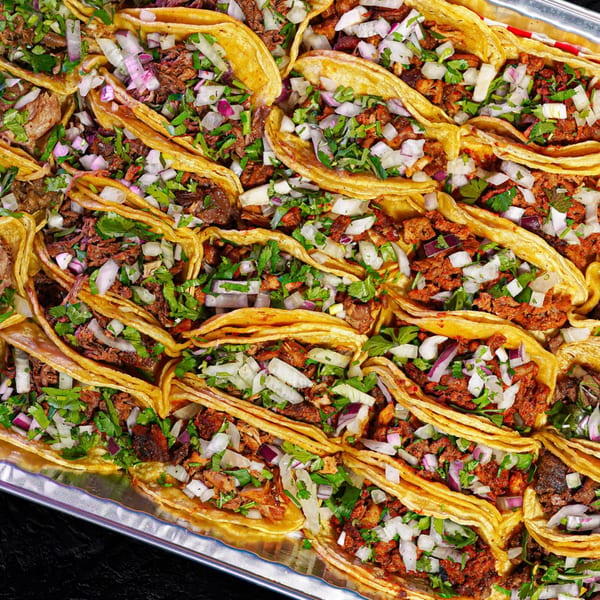A tray filled with many Quesa Loco Mexican tacos, topped with diced onions and cilantro.