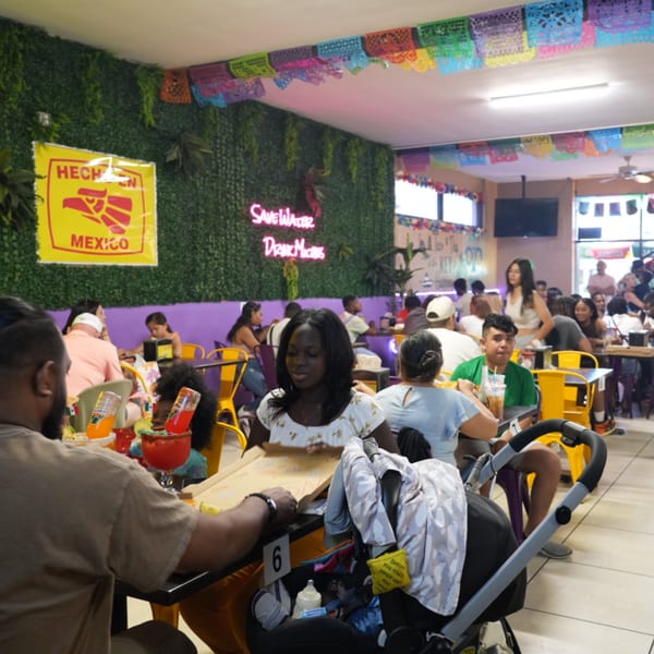 Diners enjoying meals and drinks in a lively Quesa Loco restaurant with colorful decorations.