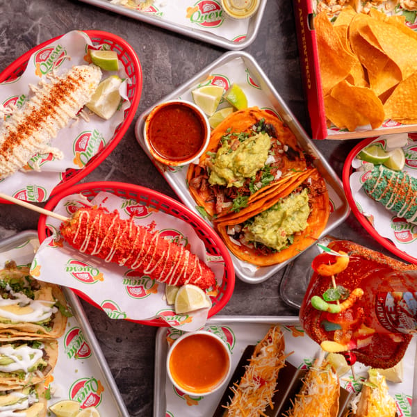 A vibrant spread of Quesa Loco's Mexican dishes, including tacos, elotes, nachos, and a michelada.