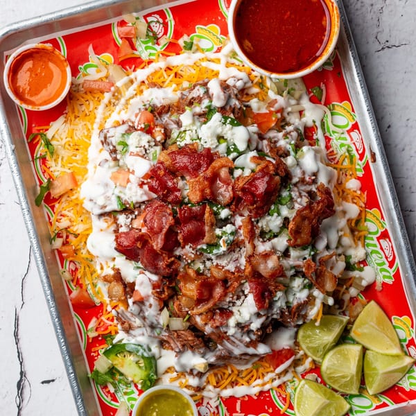 Overhead view of Quesa Loco's loaded nachos with bacon, cheese, and sauces on a red tray.