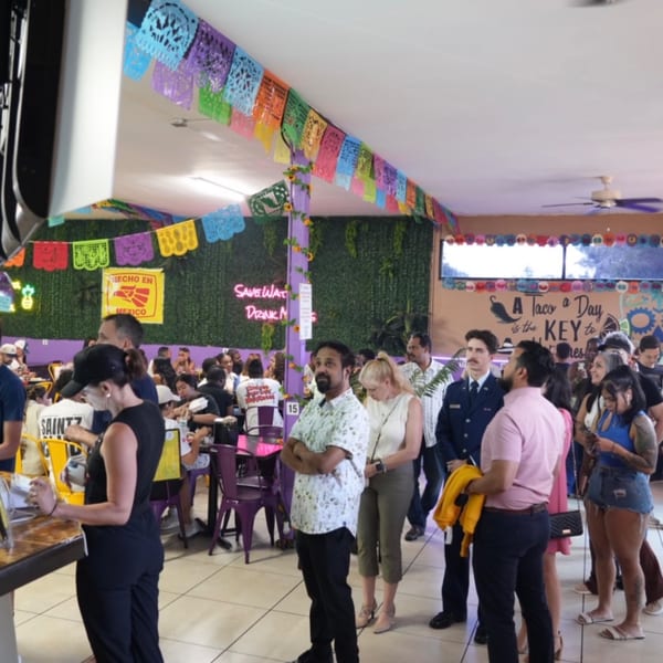 A lively Quesa Loco restaurant interior with colorful papel picado, people dining, and a line at the counter.