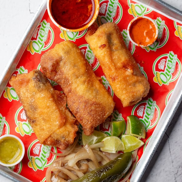Three golden-fried Quesa Loco burritos on a red tray with lime wedges, grilled onions, jalapeño, and sauces.